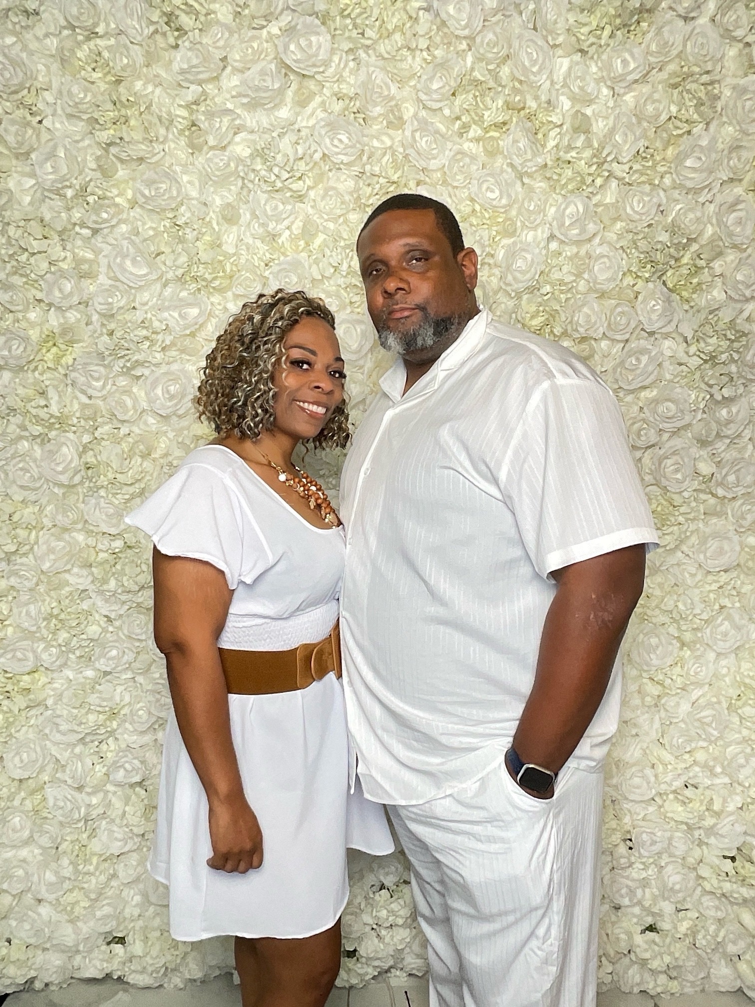 Anthony and Latisha Sims standing together in white in front of a floral wall